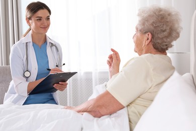 Photo of Young caregiver examining senior woman in bedroom. Home health care service