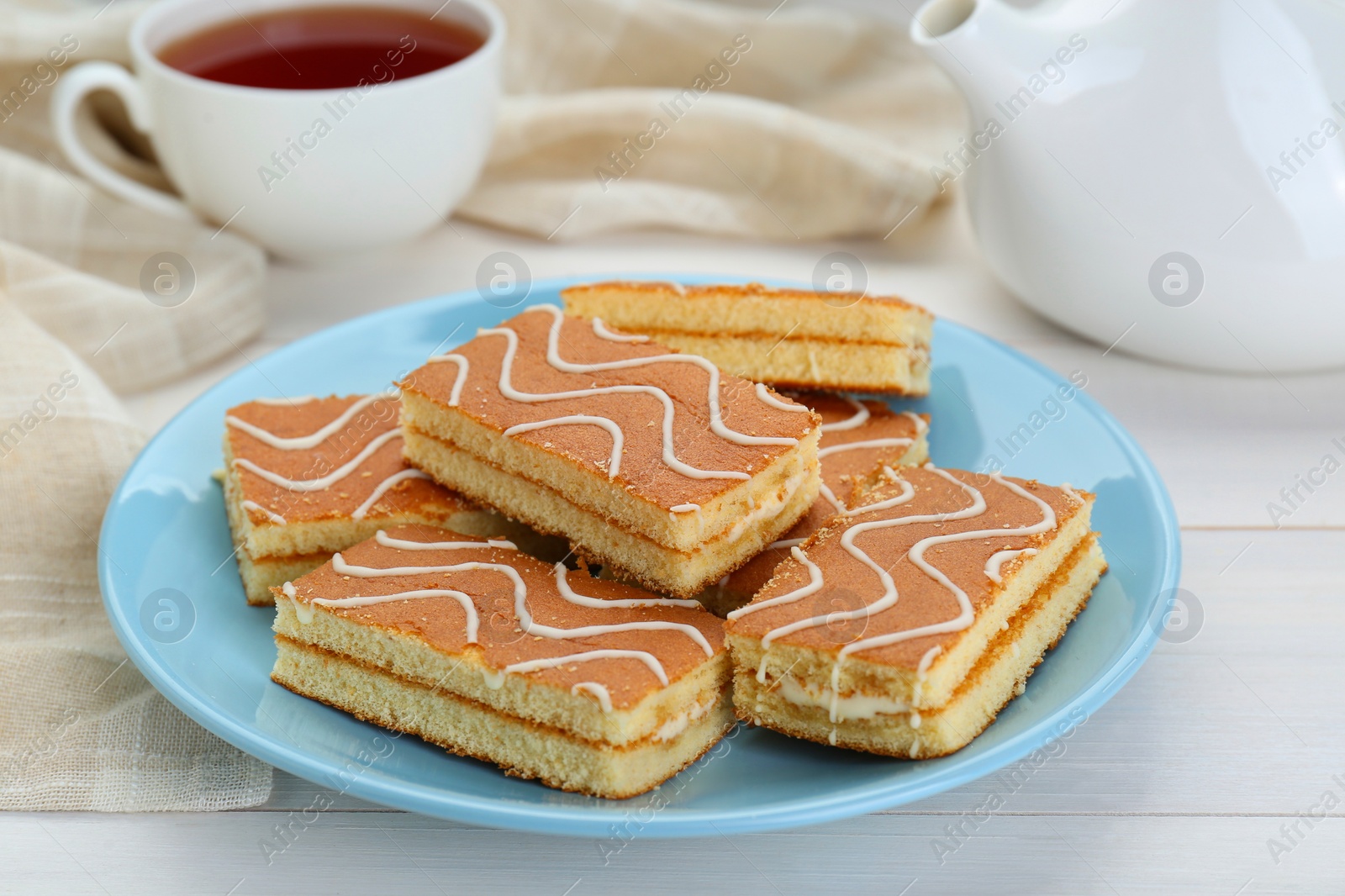 Photo of Tasty sponge cakes and hot drink on while wooden table