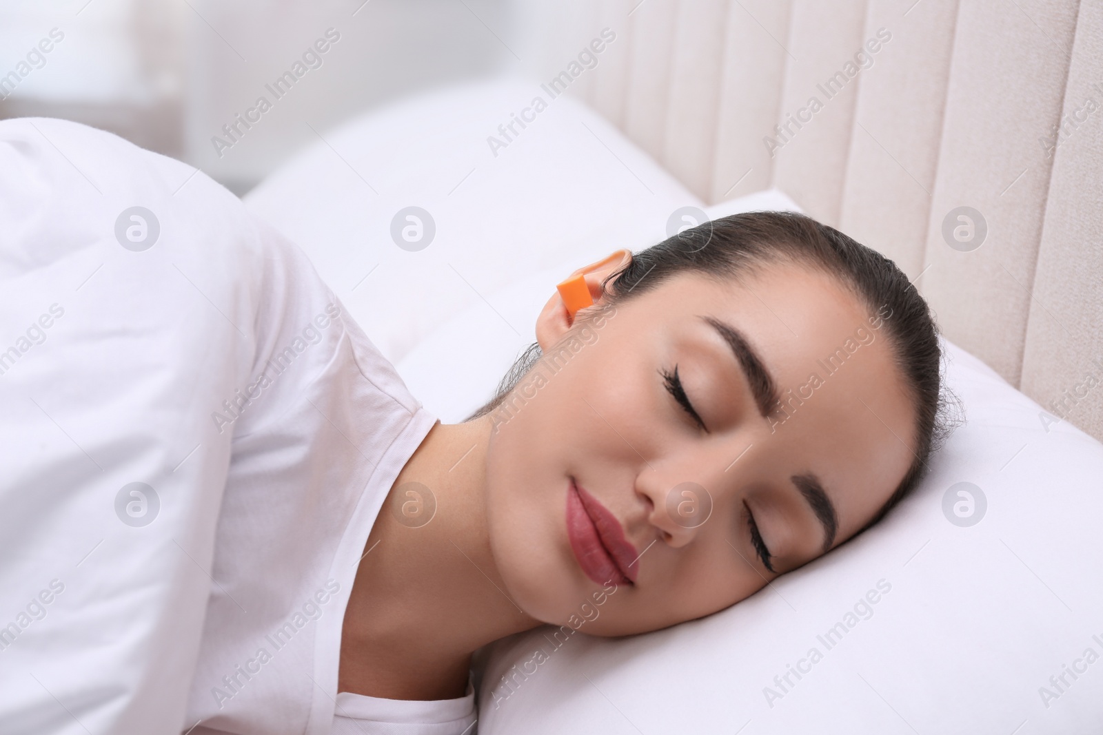 Photo of Young woman with foam ear plugs sleeping in bed