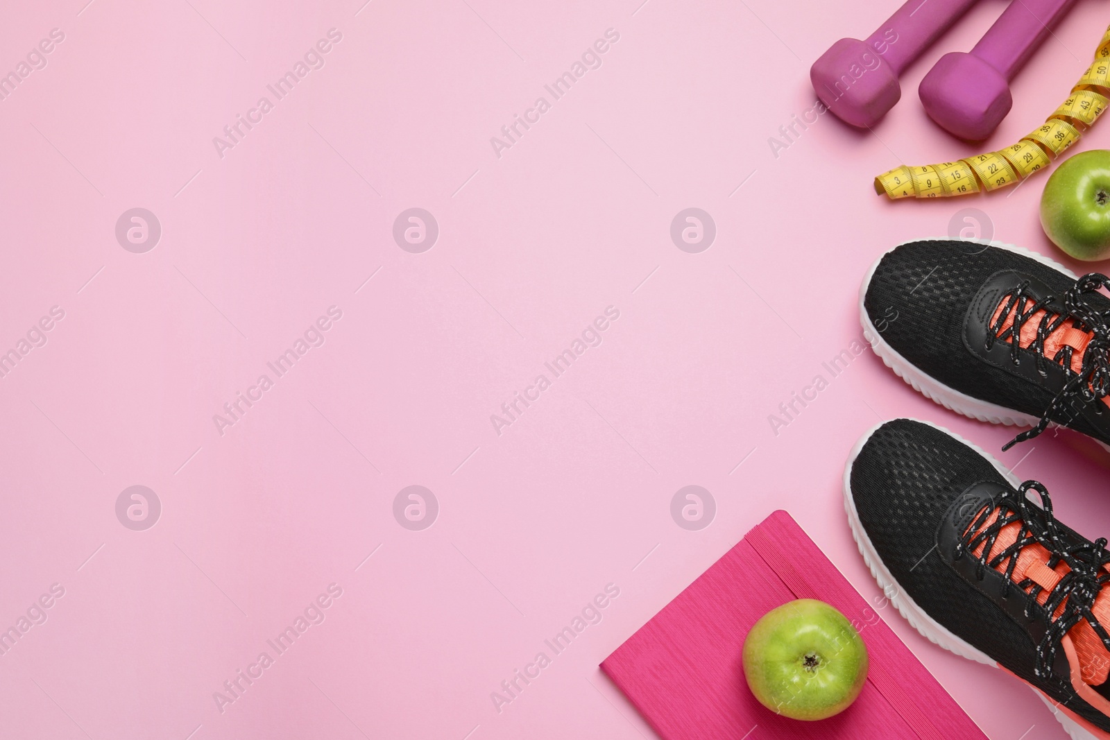 Photo of Weight loss concept. Flat lay composition with sneakers, fitness items and apples on pink background, space for text