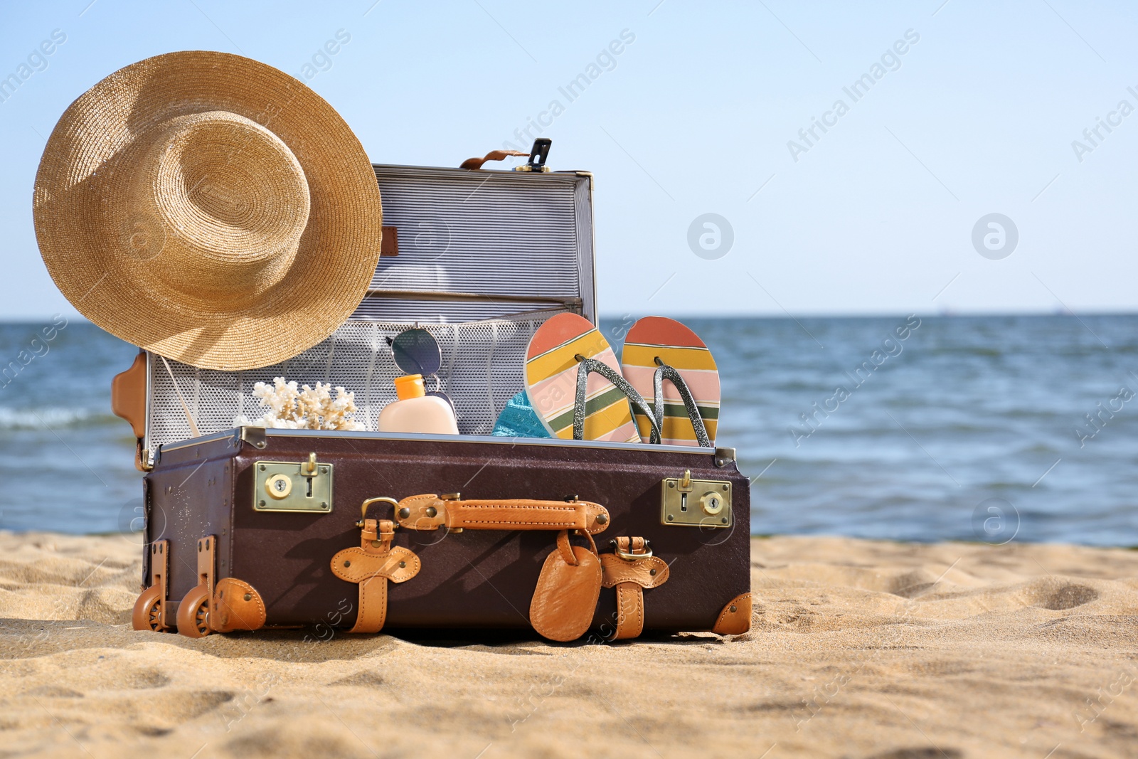 Photo of Open suitcase with stylish beach accessories on sand near sea. Space for text