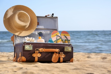 Photo of Open suitcase with stylish beach accessories on sand near sea. Space for text