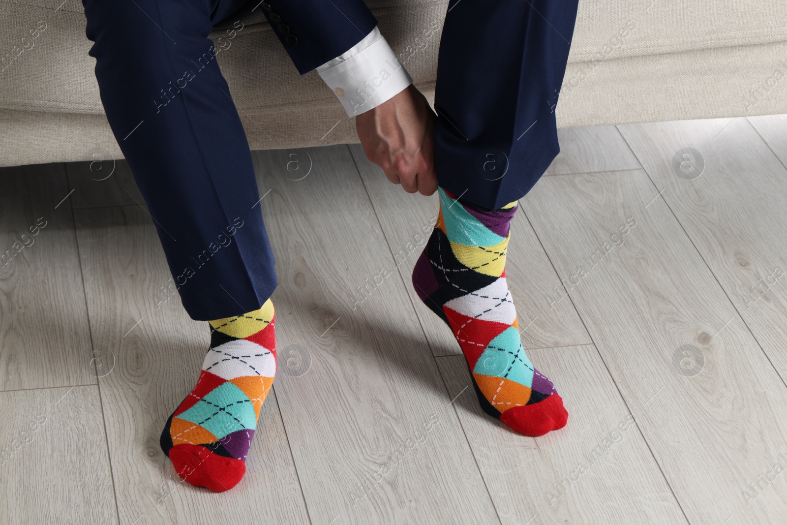 Photo of Man putting on colorful socks indoors, closeup