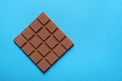 Photo of Delicious chocolate bar on light blue background, top view. Space for text