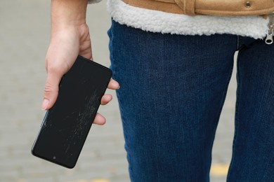 Woman holding damaged smartphone outdoors, closeup. Device repairing