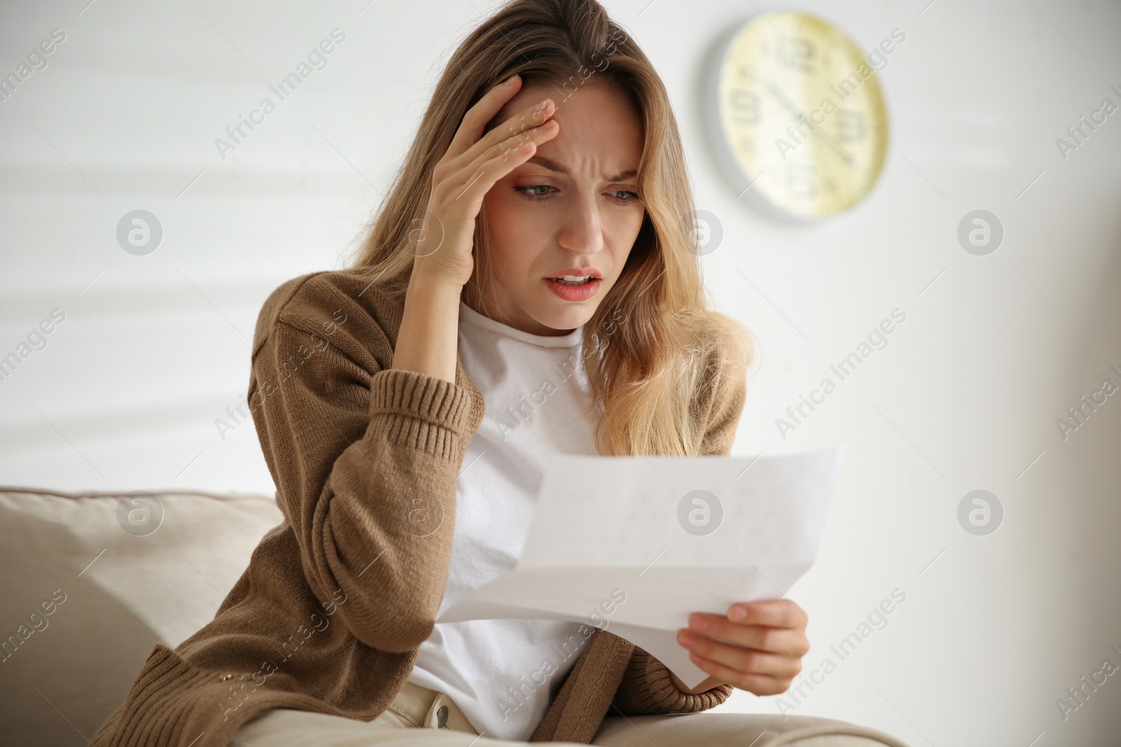 Photo of Worried woman reading letter on sofa at home