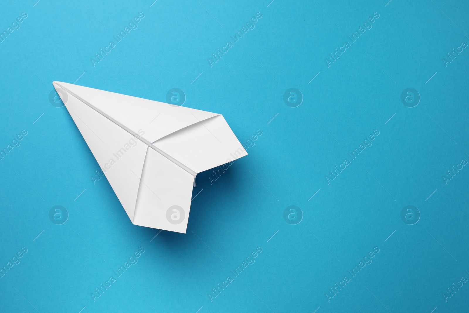 Photo of Handmade white paper plane on light blue background, top view. Space for text