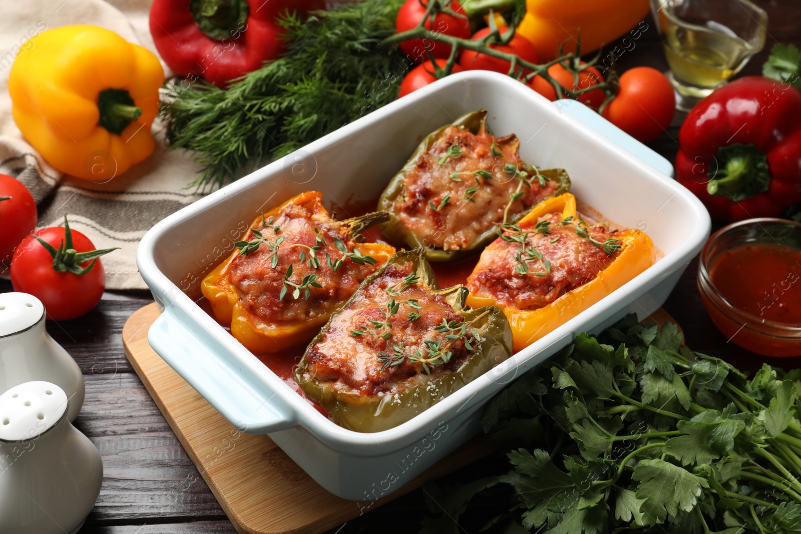 Photo of Tasty stuffed peppers in dish and ingredients on wooden table