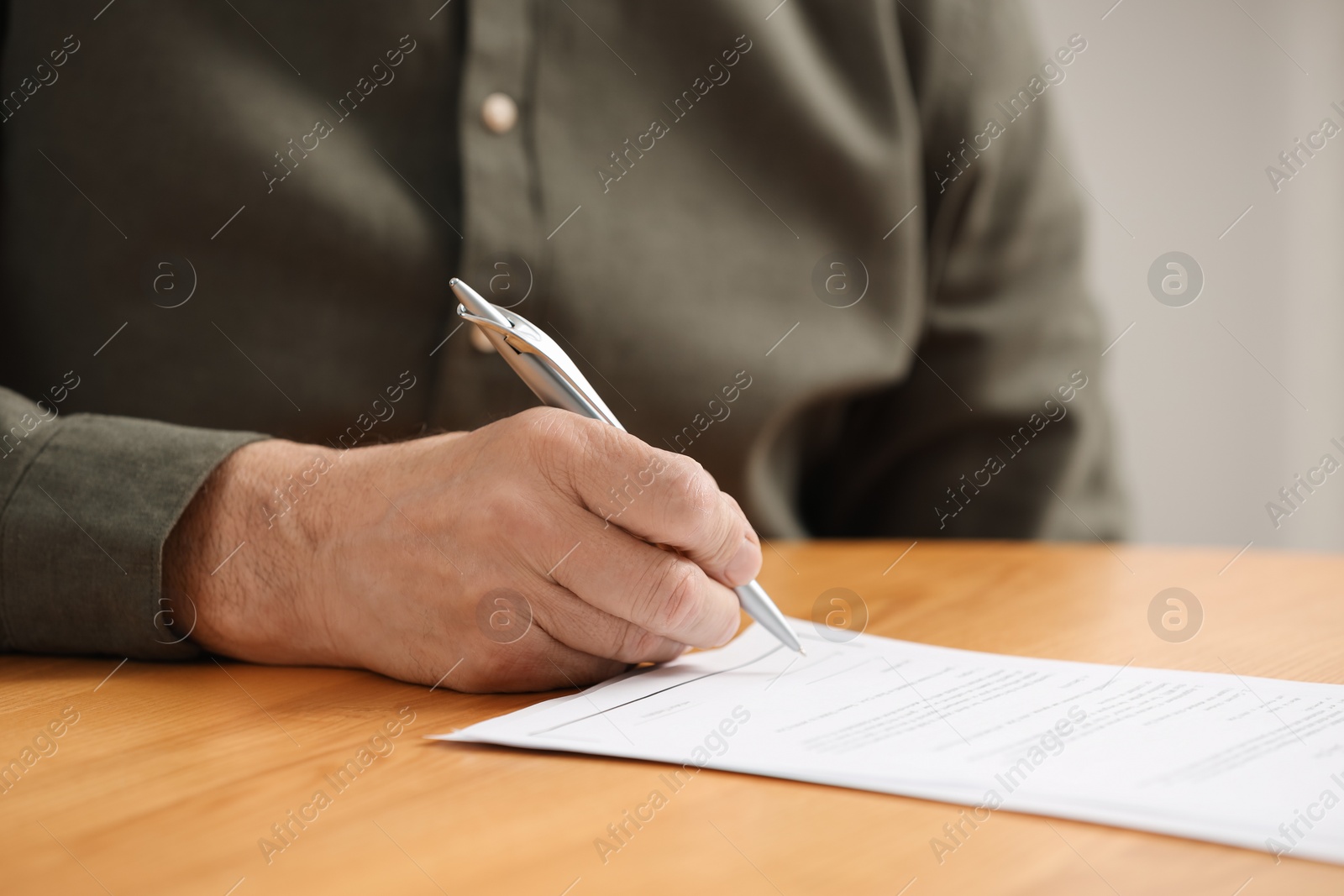 Photo of Senior man signing Last Will and Testament at wooden table indoors, closeup