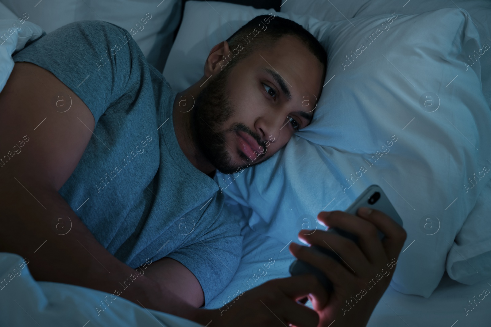 Photo of Young man using smartphone in bed at night. Internet addiction