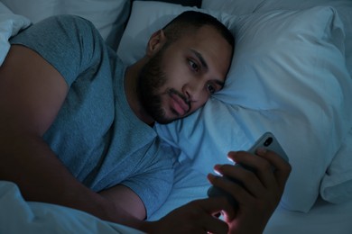 Photo of Young man using smartphone in bed at night. Internet addiction