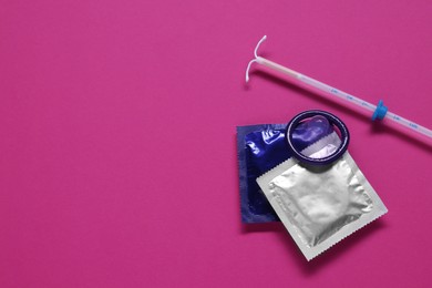 Condoms and intrauterine device on pink background, flat lay and space for text. Choosing contraceptive method