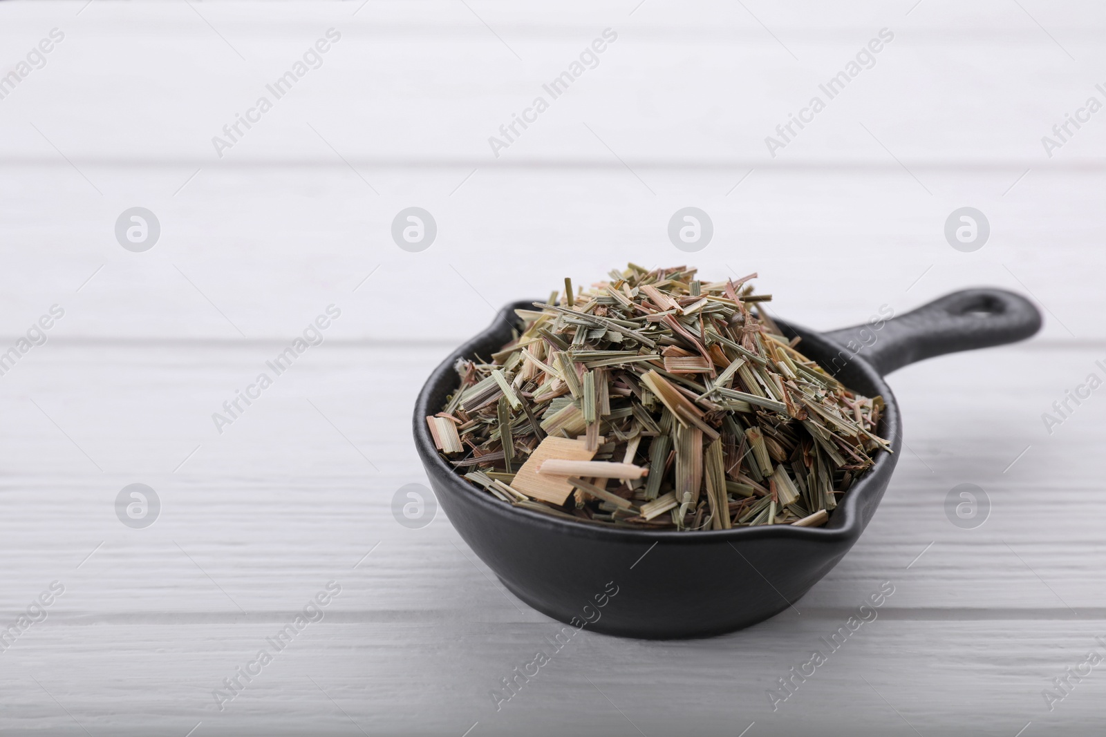 Photo of Small saucepan with aromatic dried lemongrass on white wooden table. Space for text