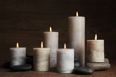 Photo of Burning candles and spa stones on wooden table