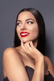 Portrait of beautiful young woman with red glossy lips on gray background