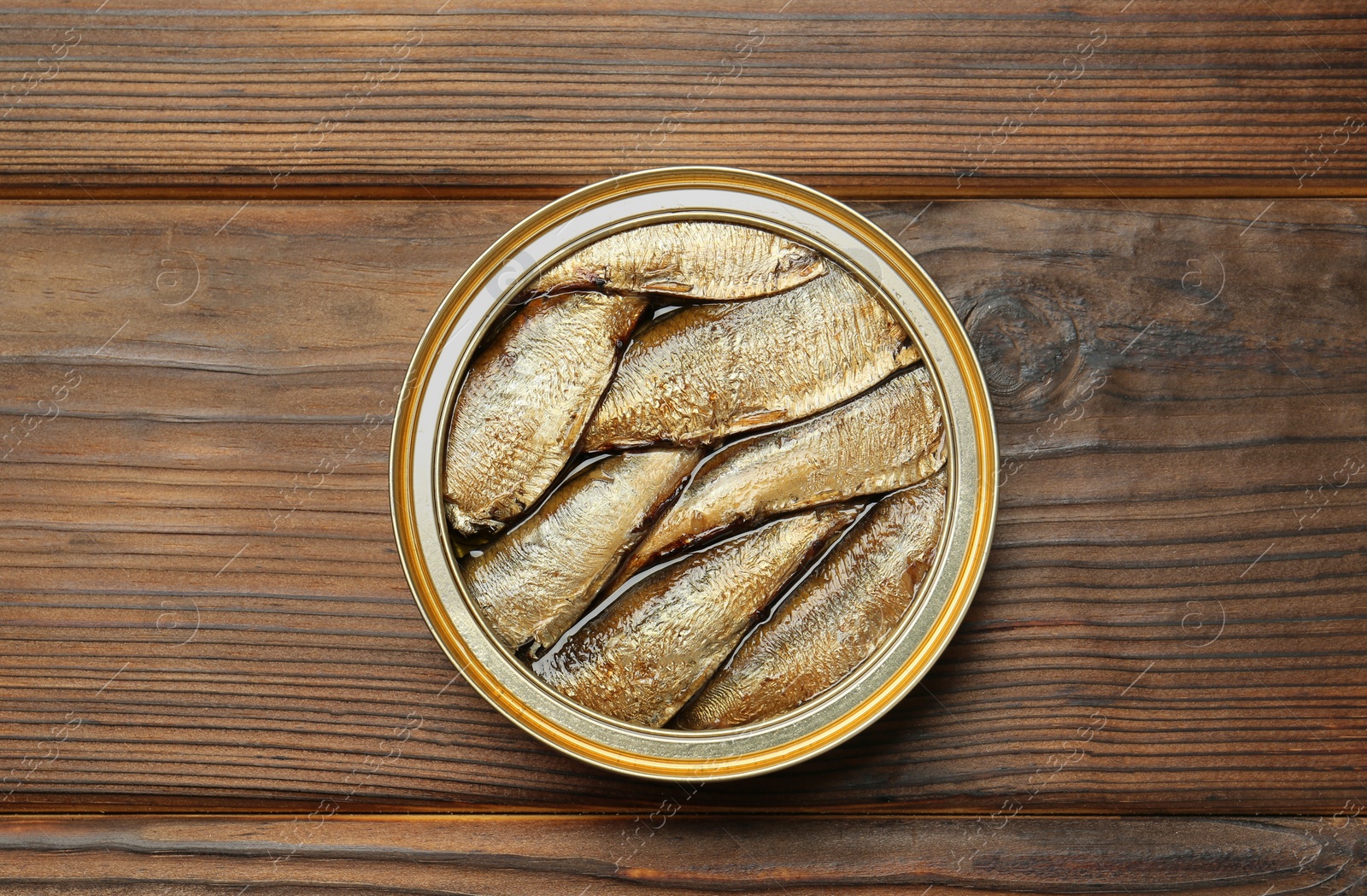 Photo of Open tin can of sprats on wooden table, top view