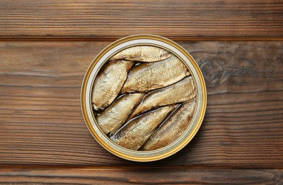 Photo of Open tin can of sprats on wooden table, top view