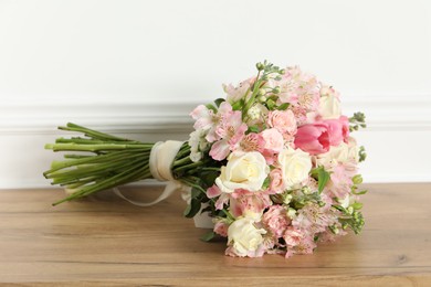 Beautiful bouquet of fresh flowers on wooden table near white wall