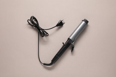 Photo of Curling iron on beige background, top view