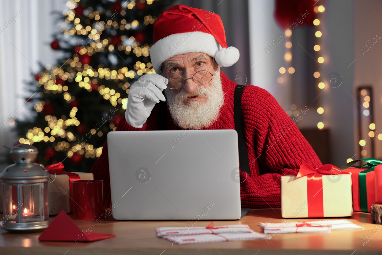 Photo of Emotional Santa Claus using laptop at his workplace in room with Christmas tree