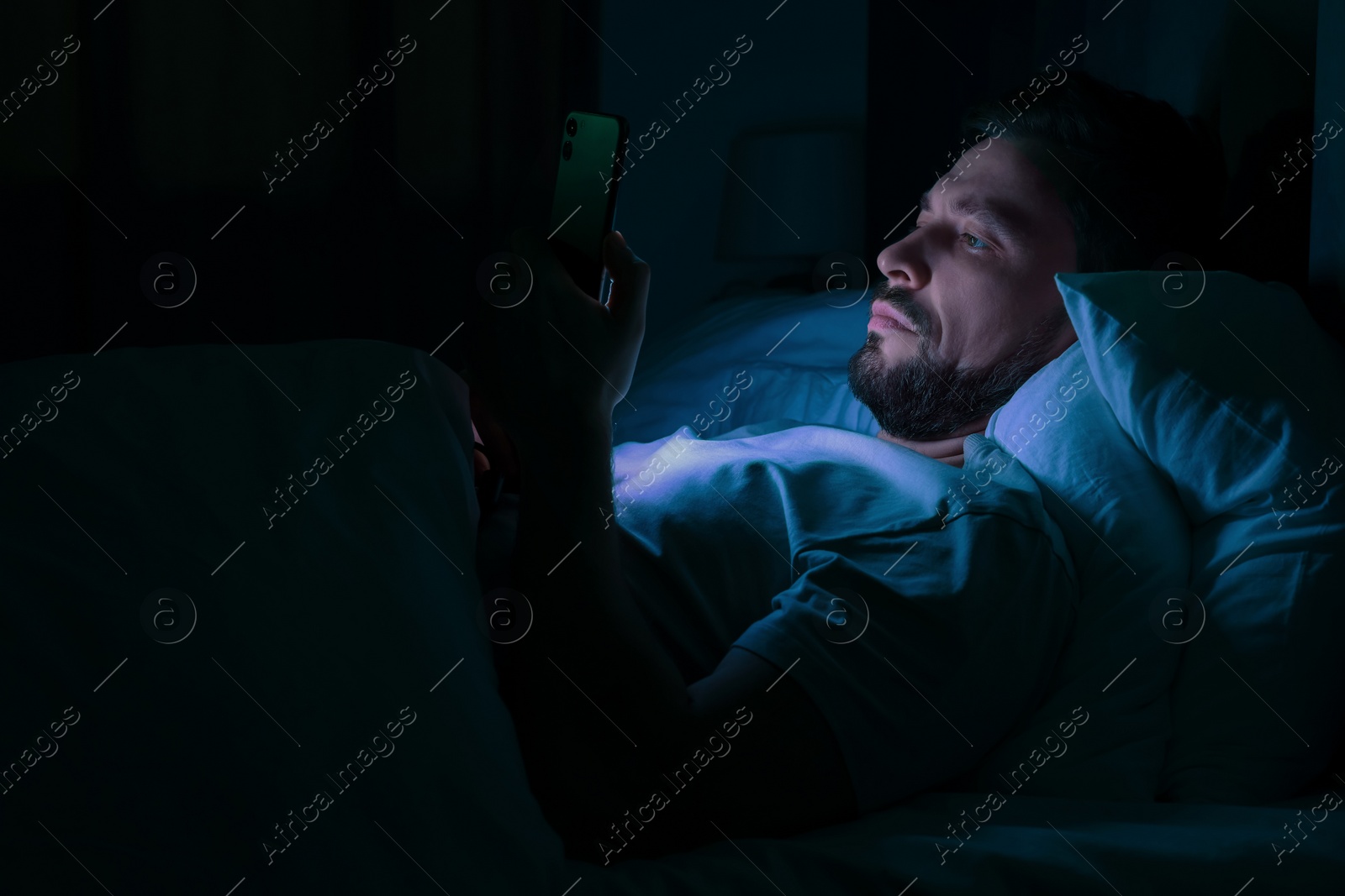 Photo of Man using smartphone in bed at night. Internet addiction