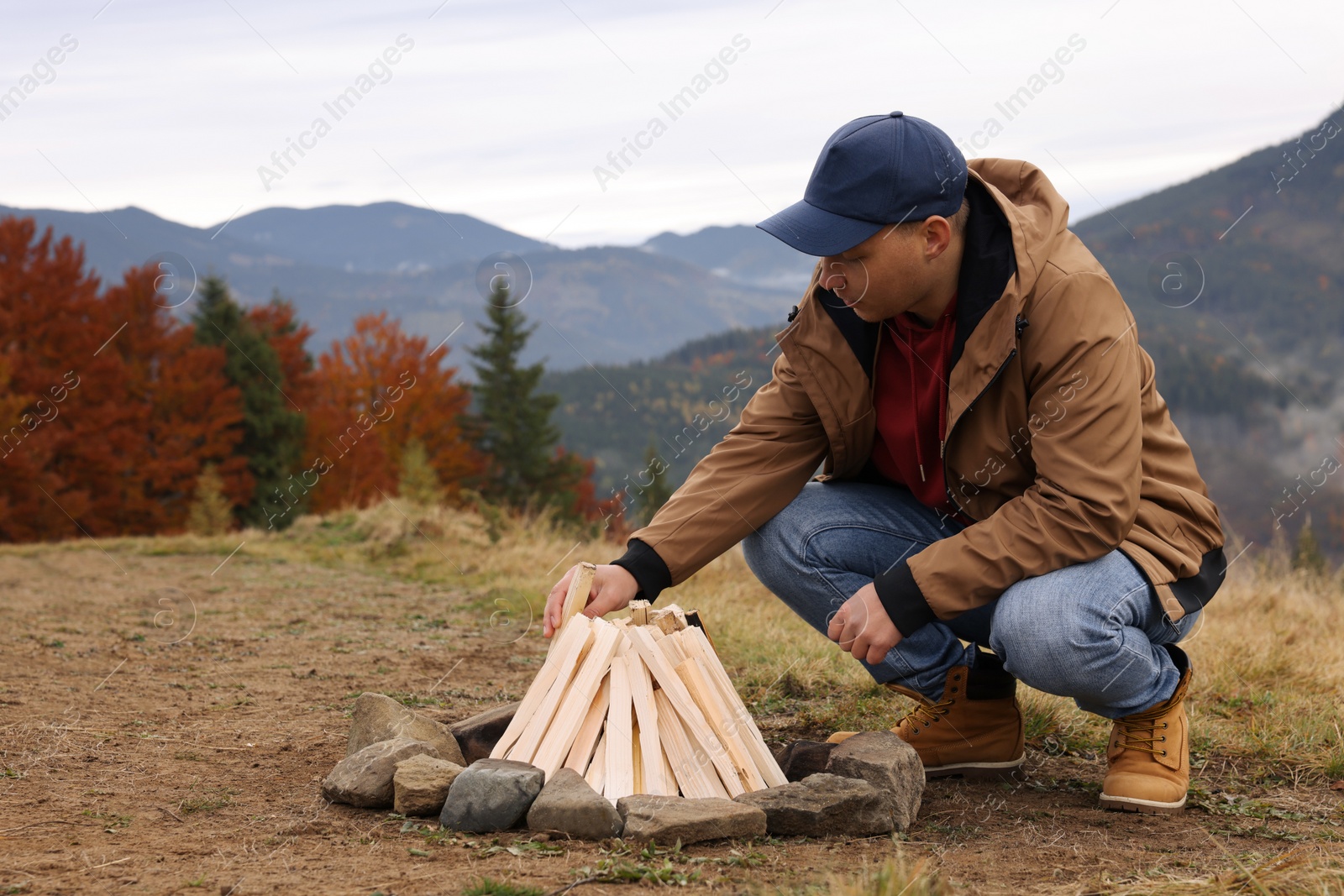 Photo of Young man making bonfire in mountains. Camping season