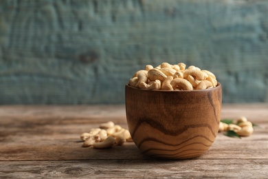 Photo of Tasty cashew nuts in bowl on wooden table. Space for text