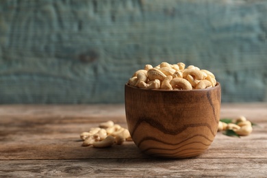 Tasty cashew nuts in bowl on wooden table. Space for text