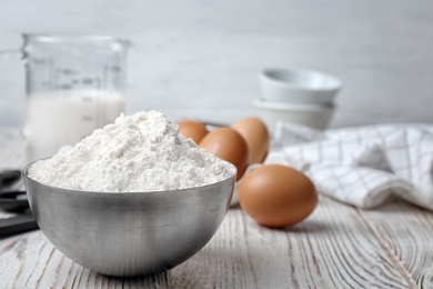 Photo of Bowl with flour on wooden table