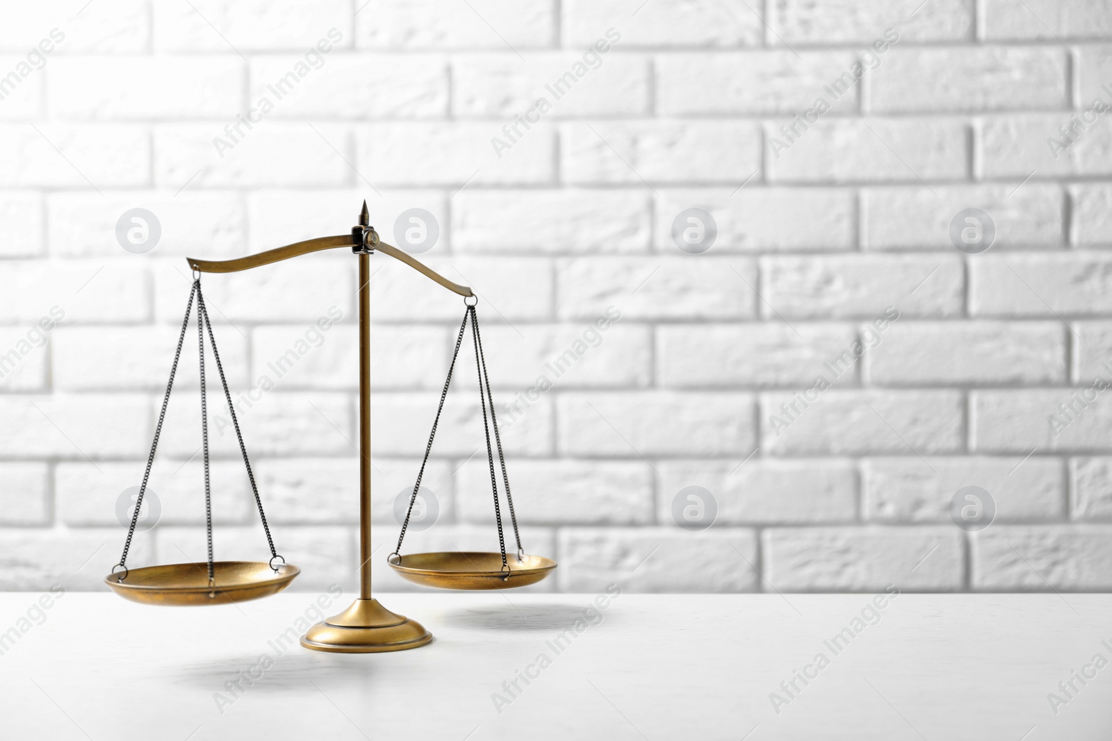 Photo of Scales of justice on table against brick wall. Law concept