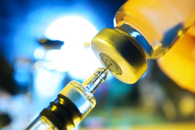 Filling syringe with vaccine from vial on blurred background, closeup