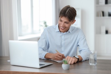 Photo of Man taking notes during webinar at wooden table indoors