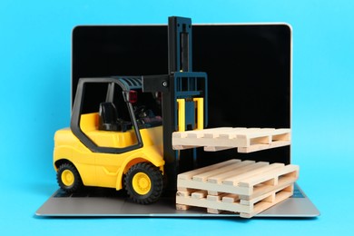 Laptop and toy forklift with wooden pallets on light blue background