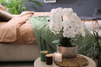 Photo of Beautiful white orchids and candles on table in bedroom, space for text. Interior design