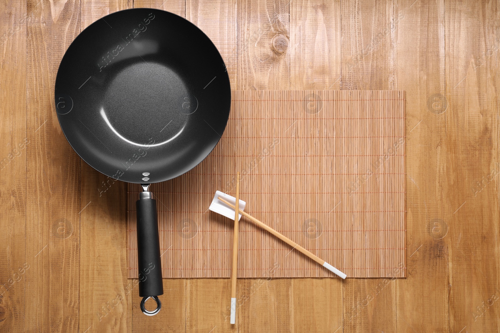 Photo of Empty iron wok and chopsticks on wooden table, top view. Space for text