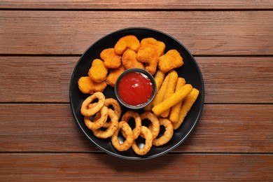 Plate with tasty ketchup and different snacks on wooden table, top view