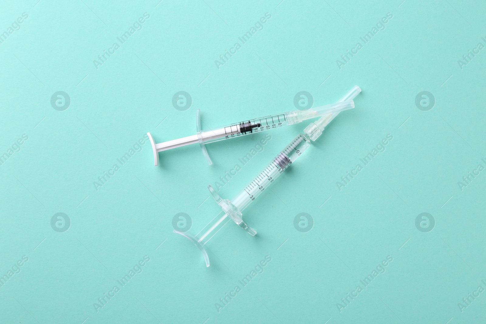 Photo of Injection cosmetology. Two medical syringes on turquoise background, top view
