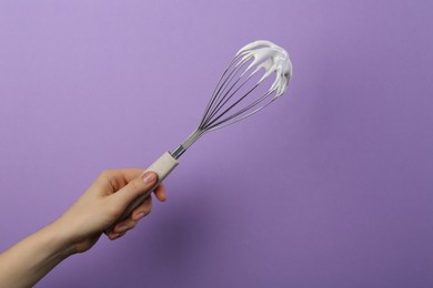 Photo of Woman holding whisk with whipped cream on violet background, closeup