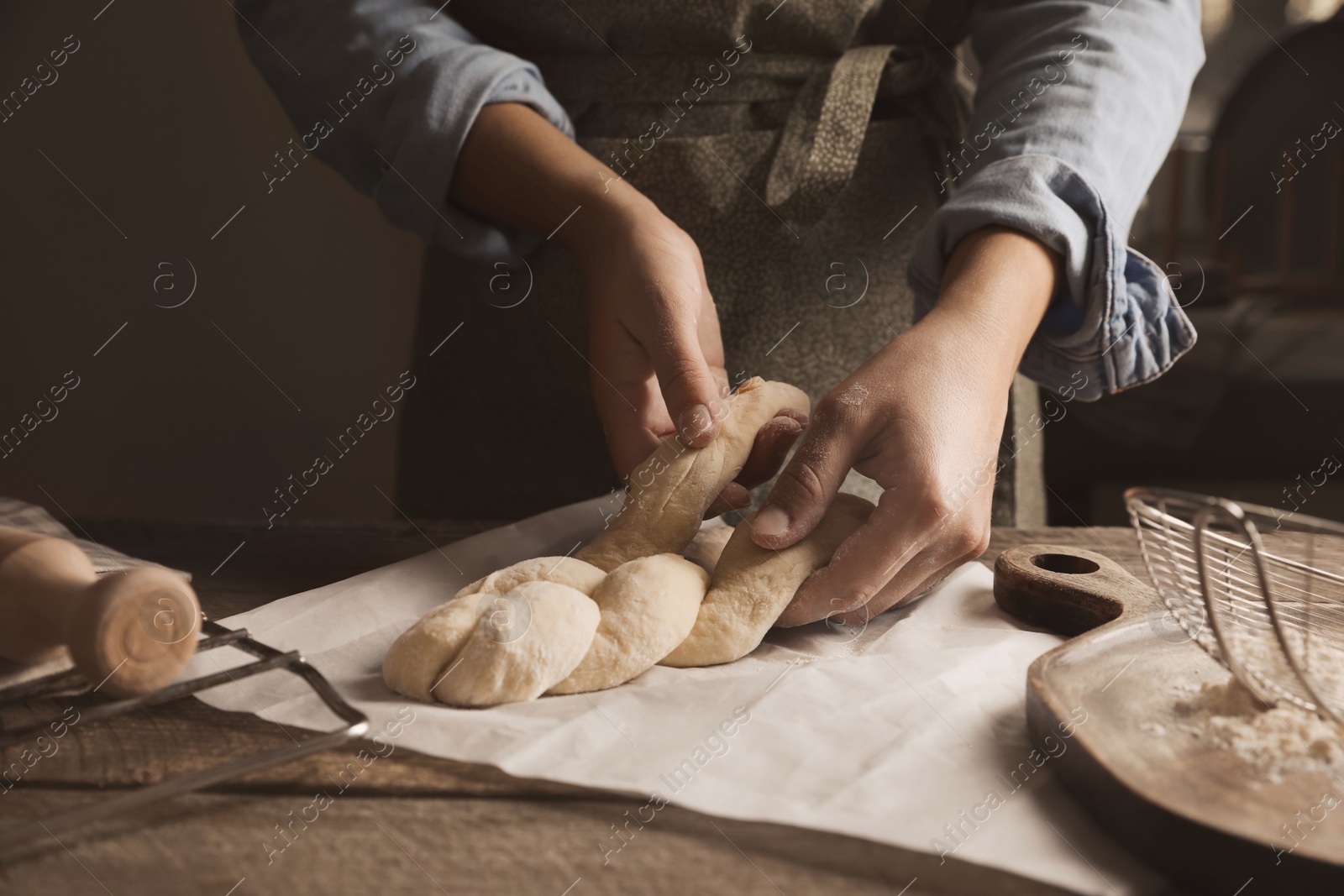 Photo of Woman making braided bread at wooden table, closeup. Traditional Shabbat challah