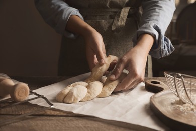 Photo of Woman making braided bread at wooden table, closeup. Traditional Shabbat challah
