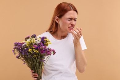 Suffering from allergy. Young woman with flowers sneezing on beige background