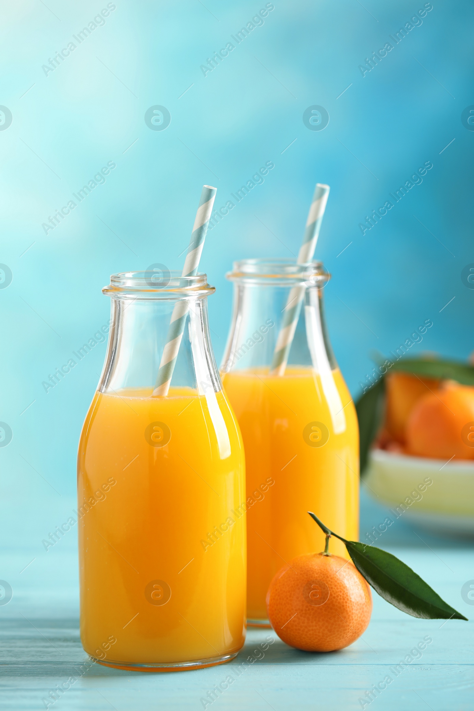 Photo of Bottles of fresh tangerine juice on blue wooden background