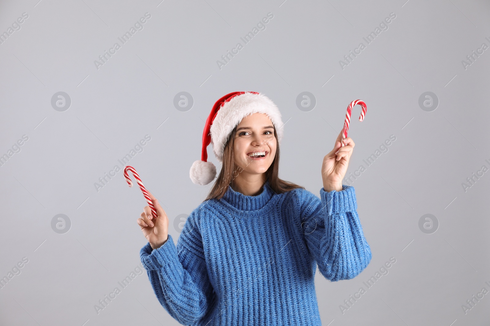 Photo of Pretty woman in Santa hat and blue sweater holding candy canes on grey background