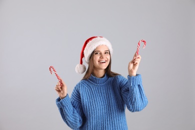 Pretty woman in Santa hat and blue sweater holding candy canes on grey background