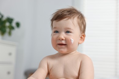 Cute little baby with moisturizing cream on face indoors