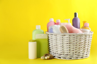Photo of Wicker basket with baby cosmetic products and accessories on yellow background
