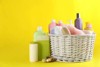 Wicker basket with baby cosmetic products and accessories on yellow background