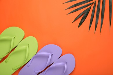 Stylish flip flops and palm leaf on orange background, flat lay. Space for text