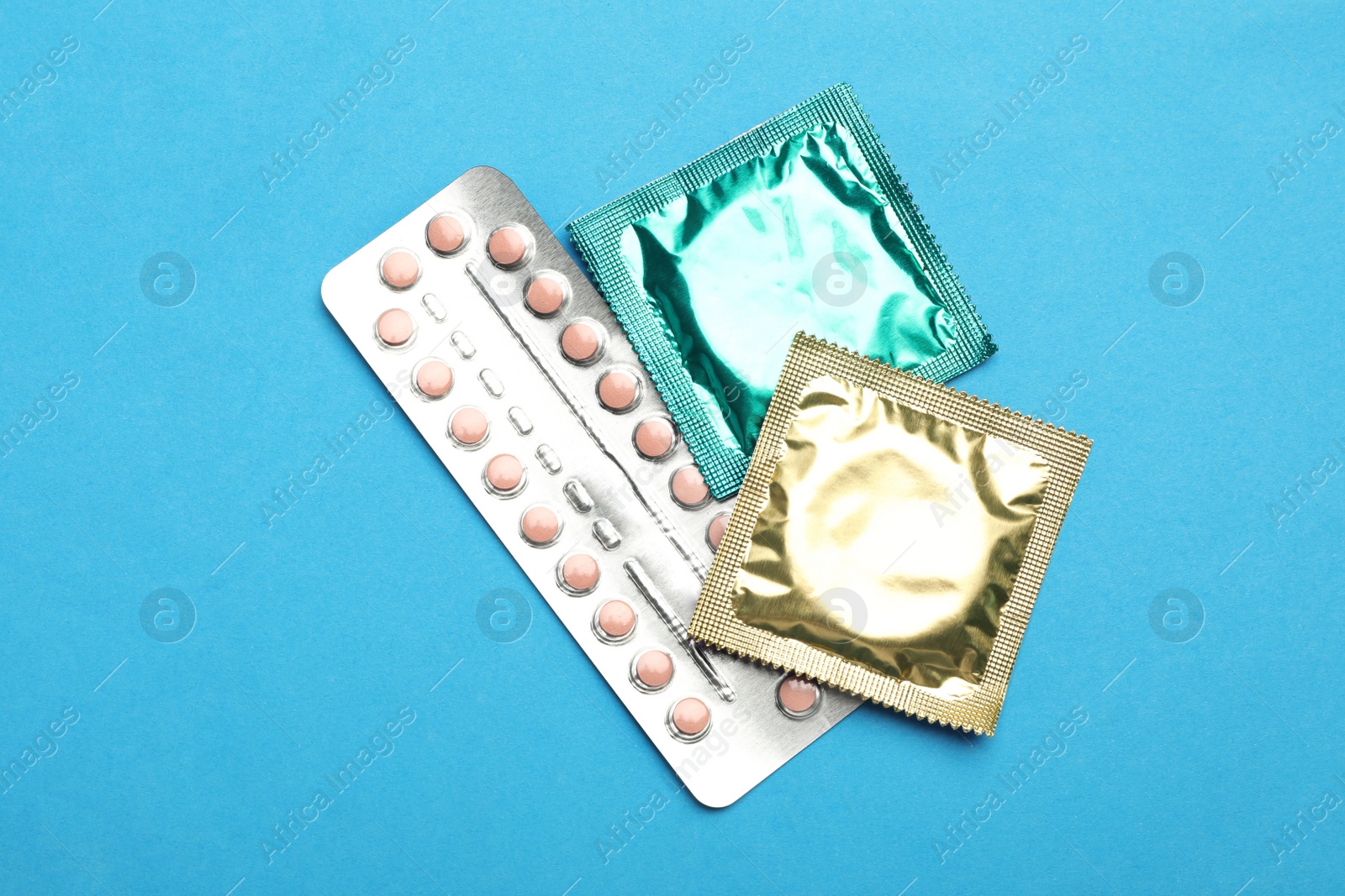 Photo of Condoms and birth control pills on light blue background, flat lay. Safe sex concept