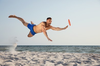 Photo of Sportive man jumping while trying to catch flying disk at beach